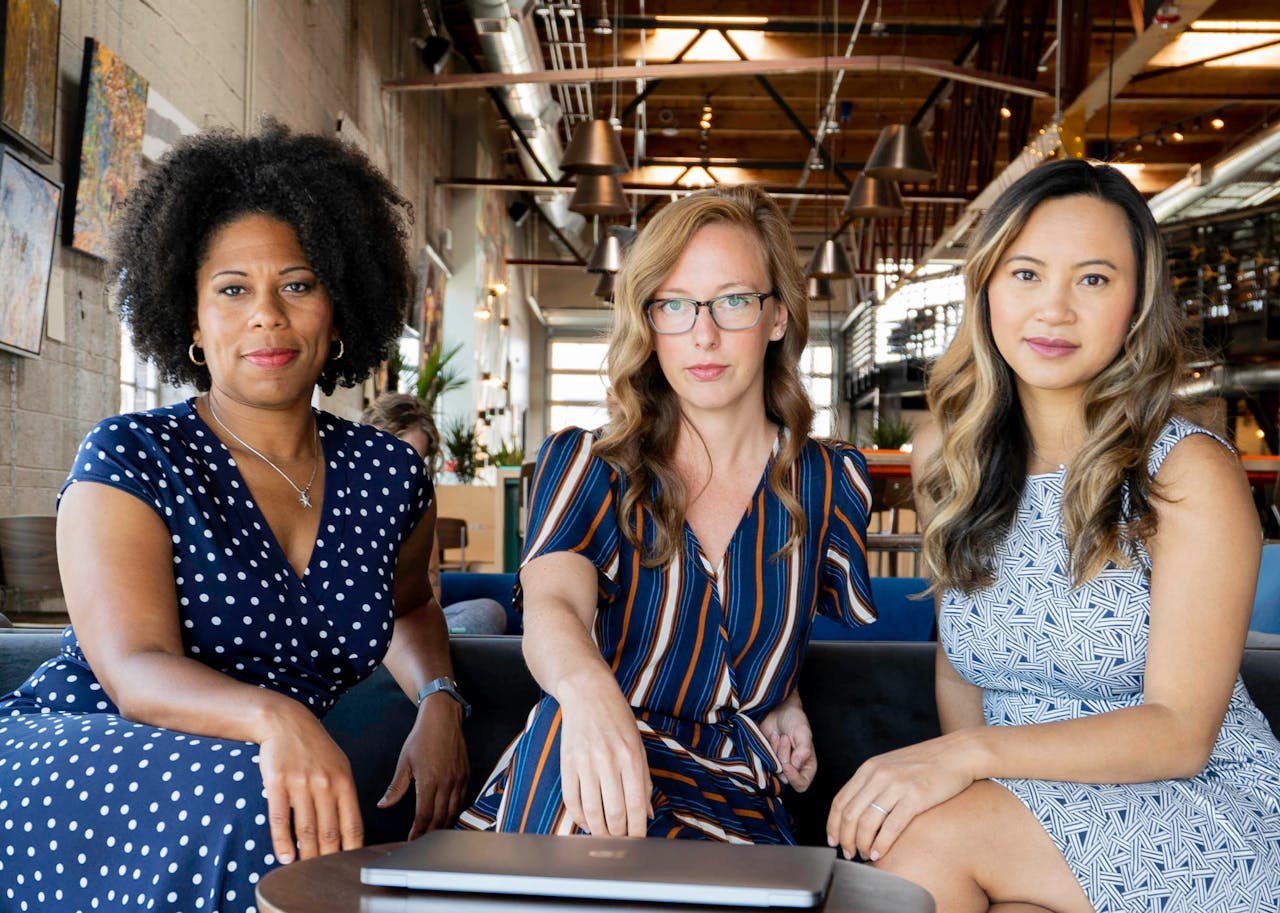 Three professional women sitting confidently in a modern office space, embracing diversity and collaboration.